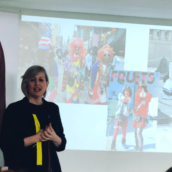 Una mujer está parada frente a una pantalla de proyección que dice frutas