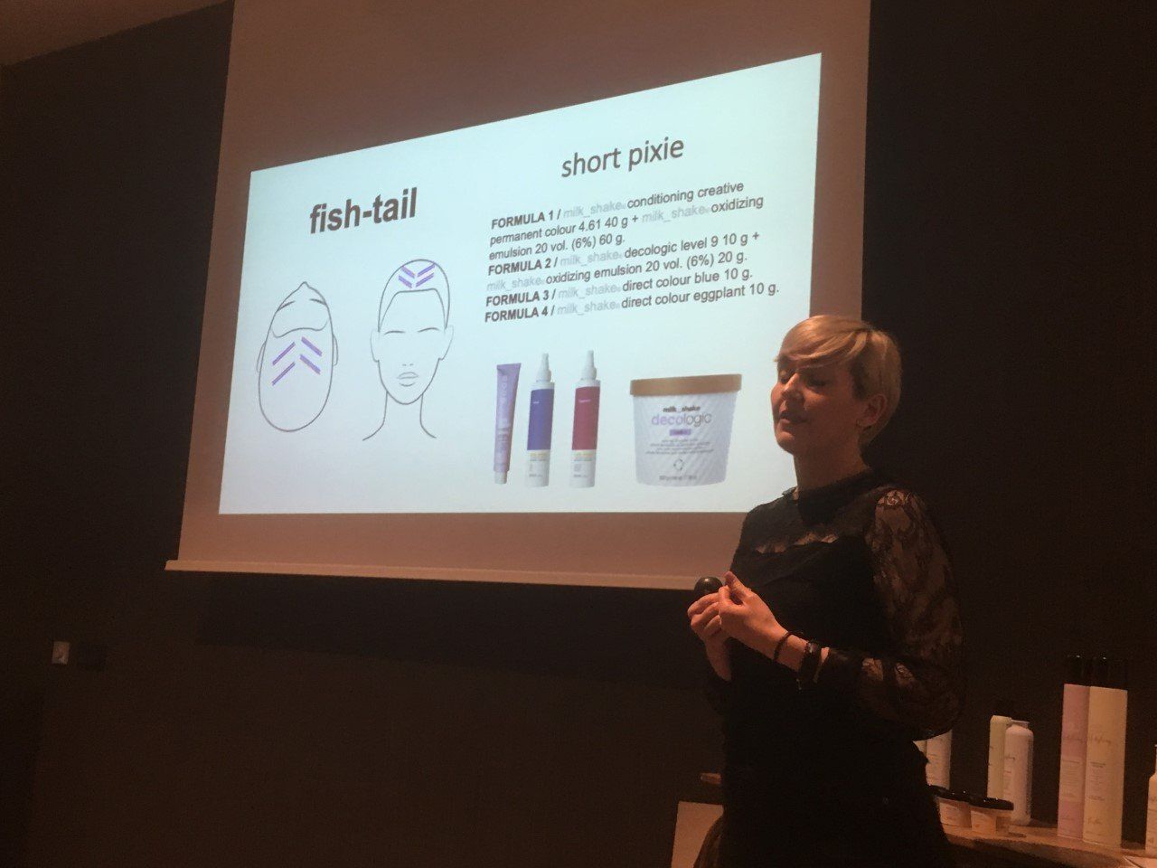 Una mujer está dando una presentación sobre cola de pez y pelo corto y pálido.