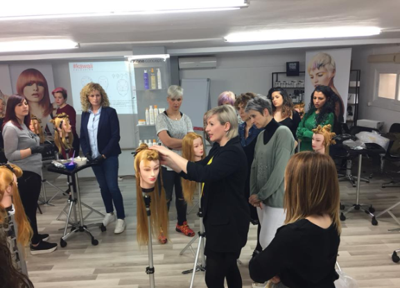 Una mujer está enseñando a un grupo de mujeres cómo cortar el cabello en maniquíes.