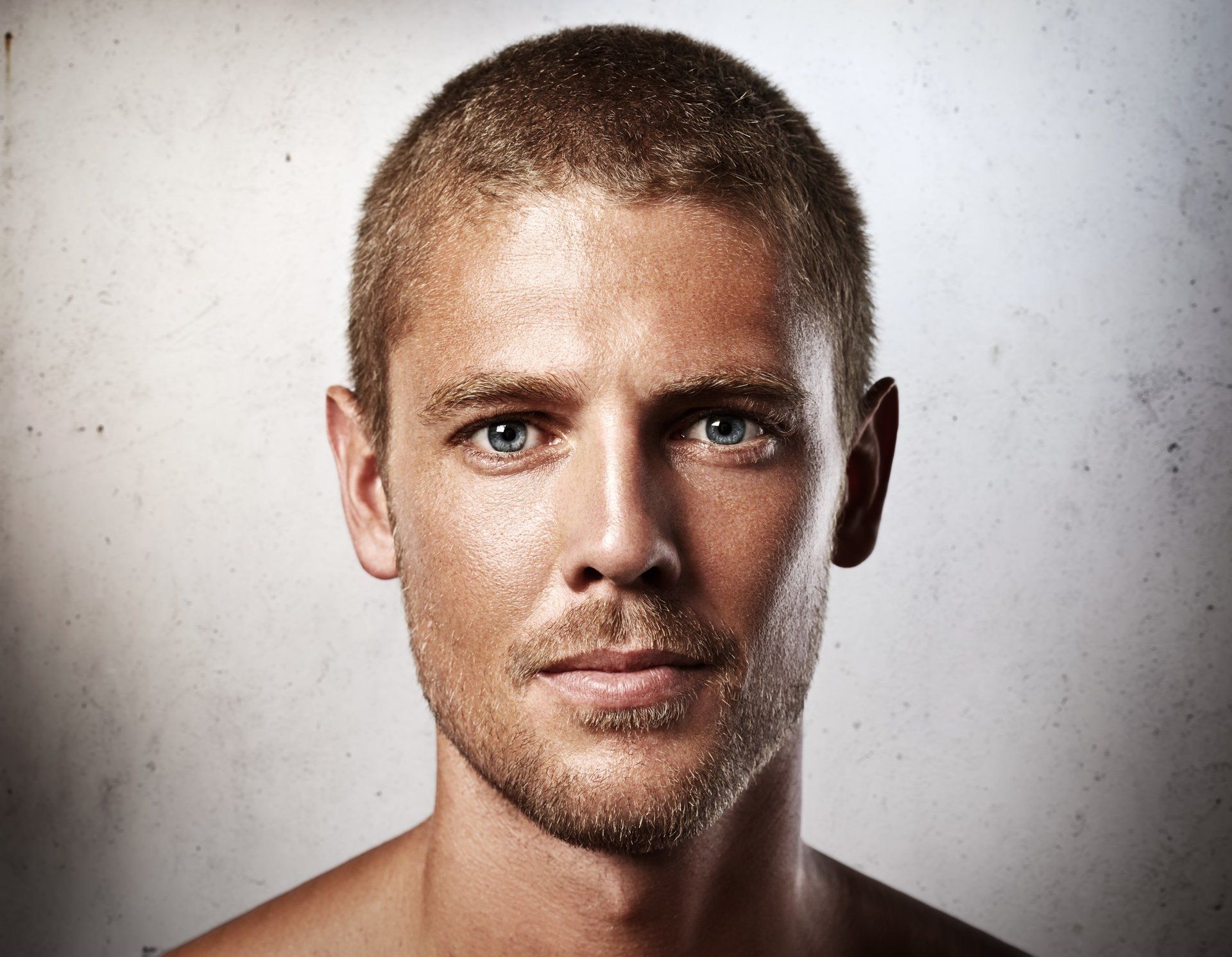 Un hombre sin camisa con barba y ojos azules mira a la cámara.