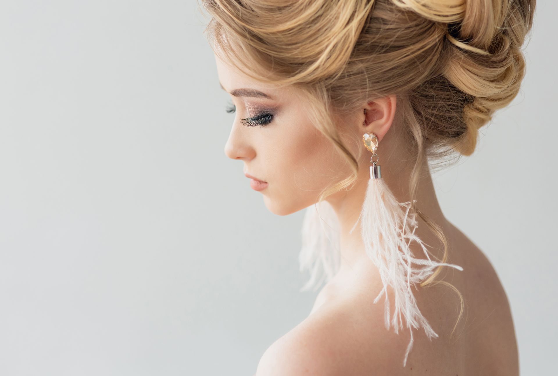 Mujer con un recogido dramático y maquillaje de ojos oscuros, de perfil sobre un fondo gris.