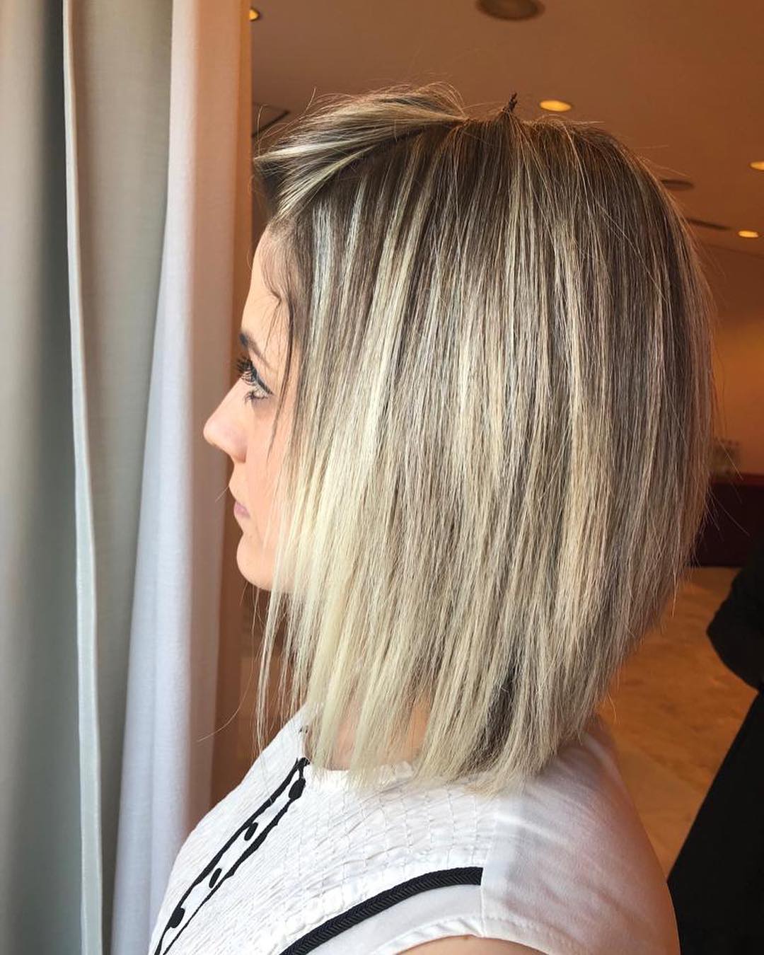 Una mujer con cabello rubio está parada frente a una ventana.