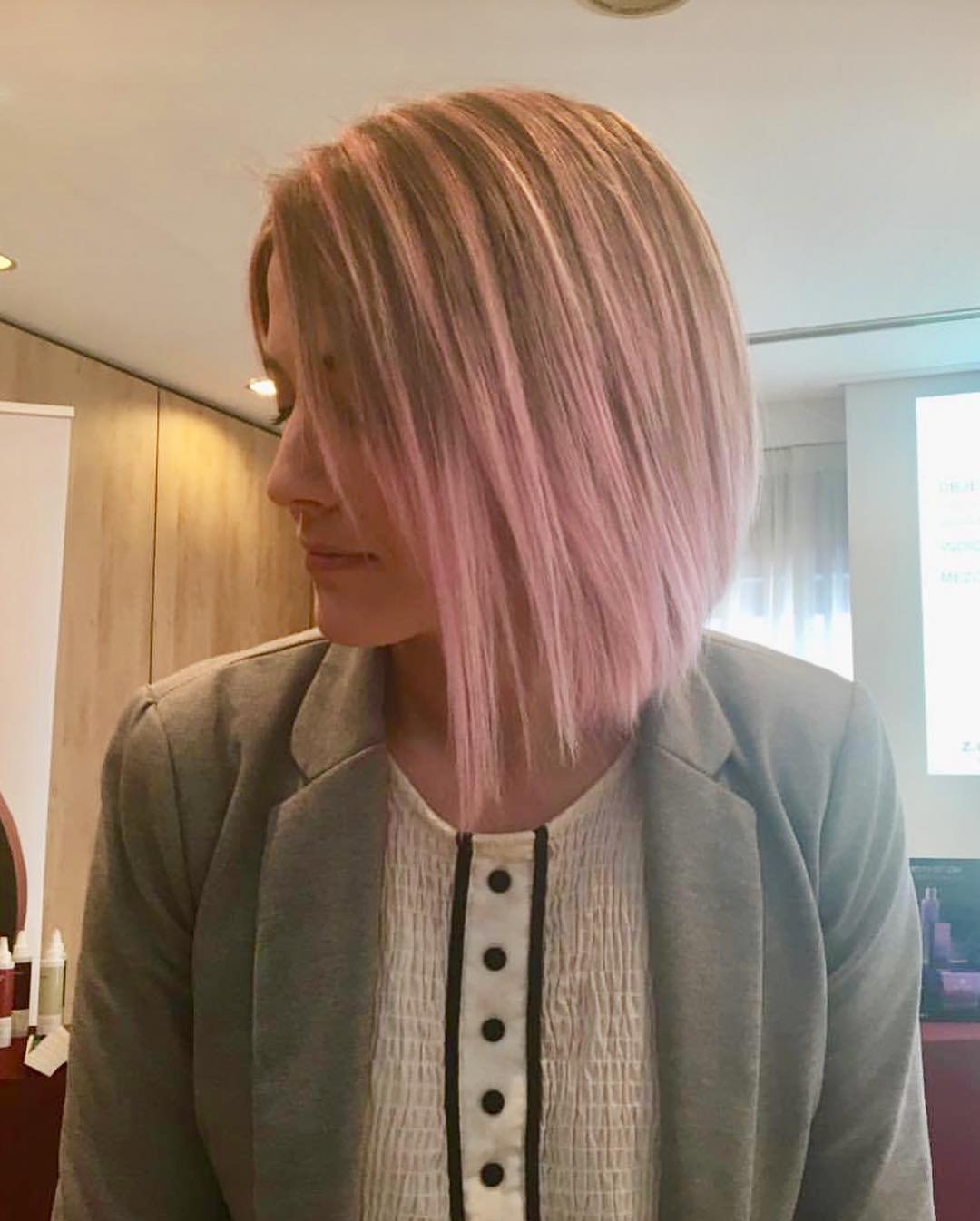 Una mujer con cabello rosa lleva una chaqueta gris y una camisa blanca.