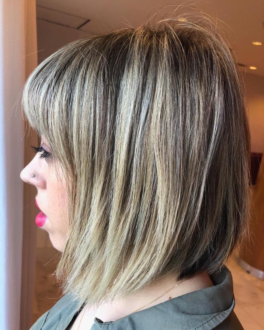 Una mujer con cabello rubio corto y flequillo lleva una camisa verde.