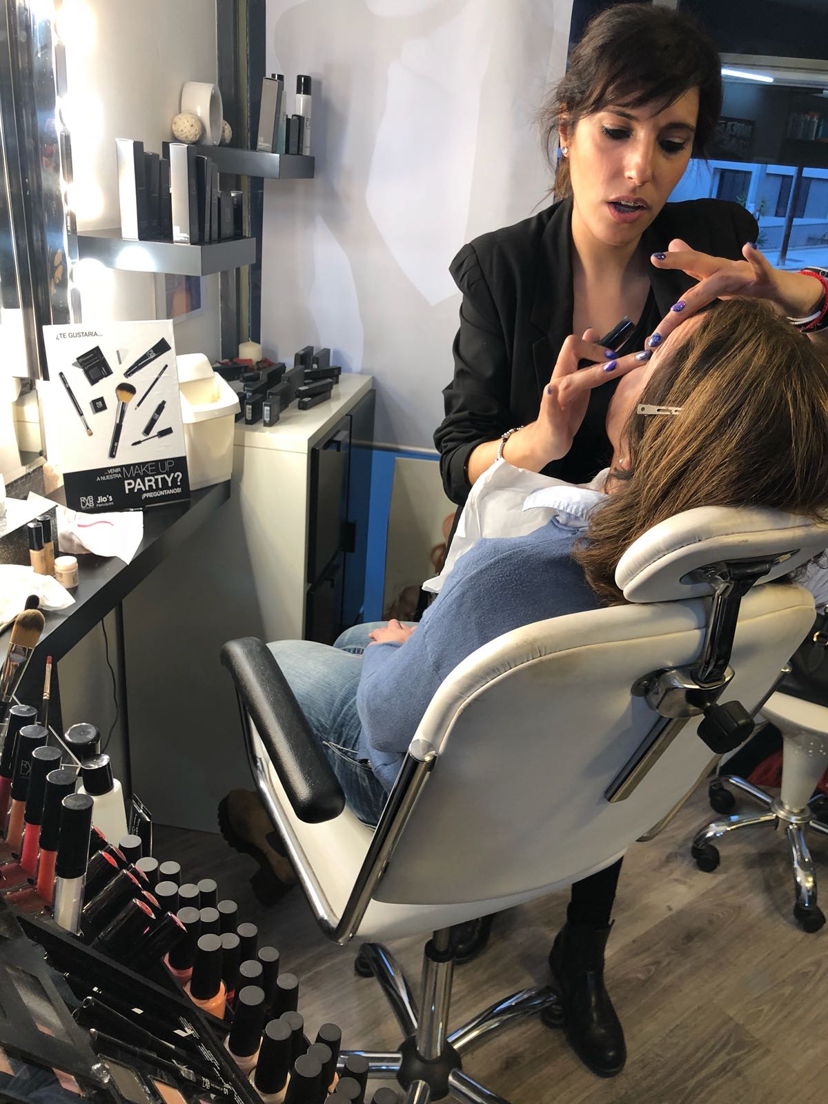 Una mujer está sentada en una silla mientras un maquillador la maquilla.