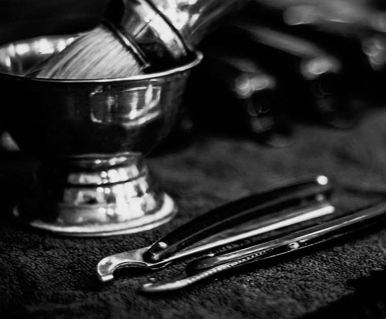 A black and white photo of a bowl of shaving brushes and razors.