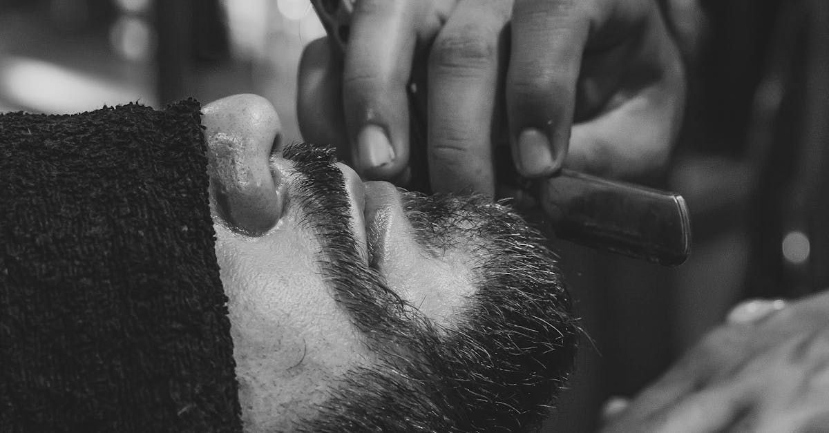 A man is getting his beard shaved by a barber in a black and white photo.