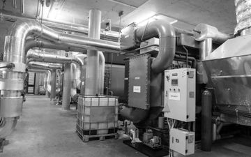 Industrial basement with large silver ductwork, pipes, and HVAC equipment beside storage crates