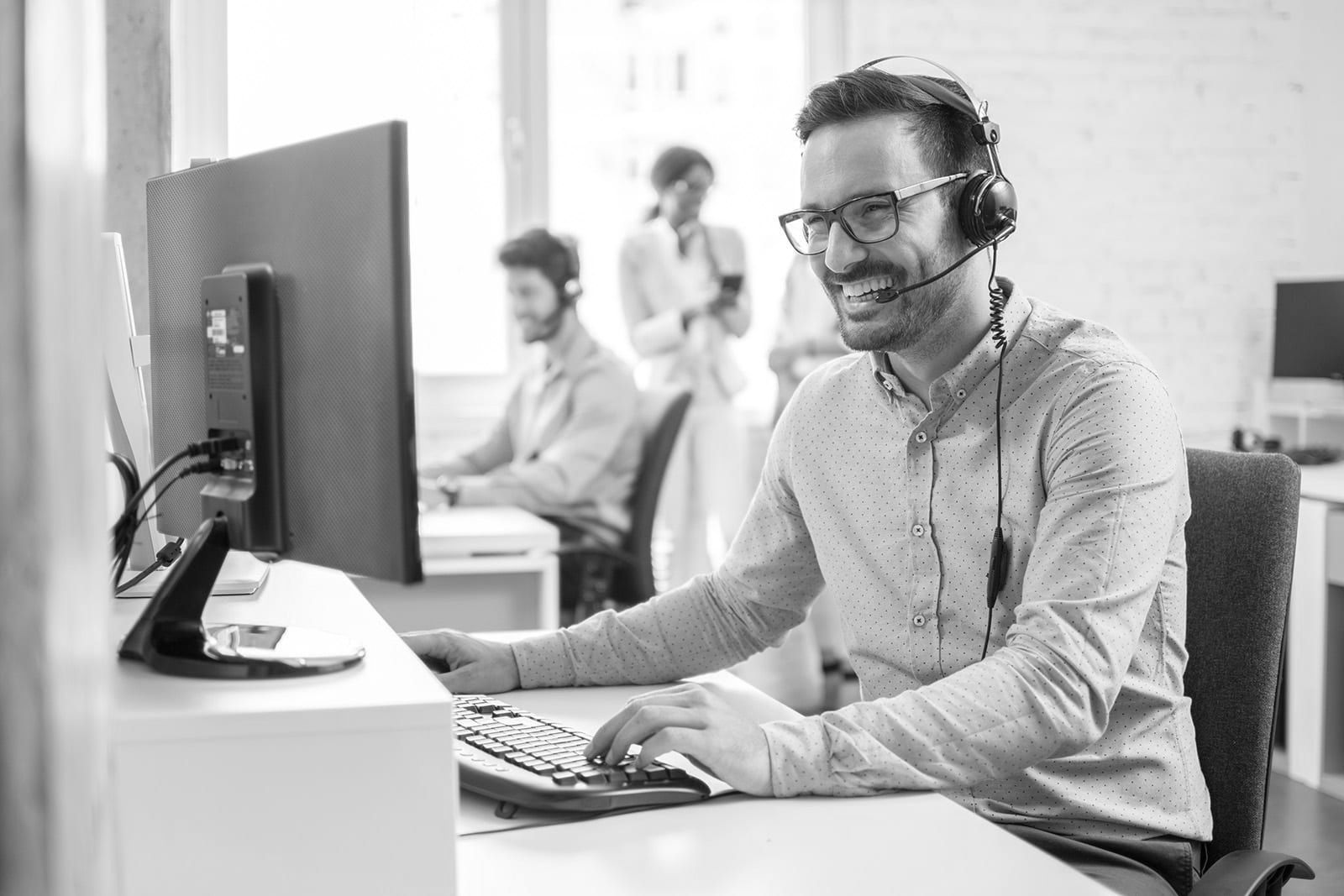 Smiling headset-wearing customer service agent at a desk with computer in a bright office