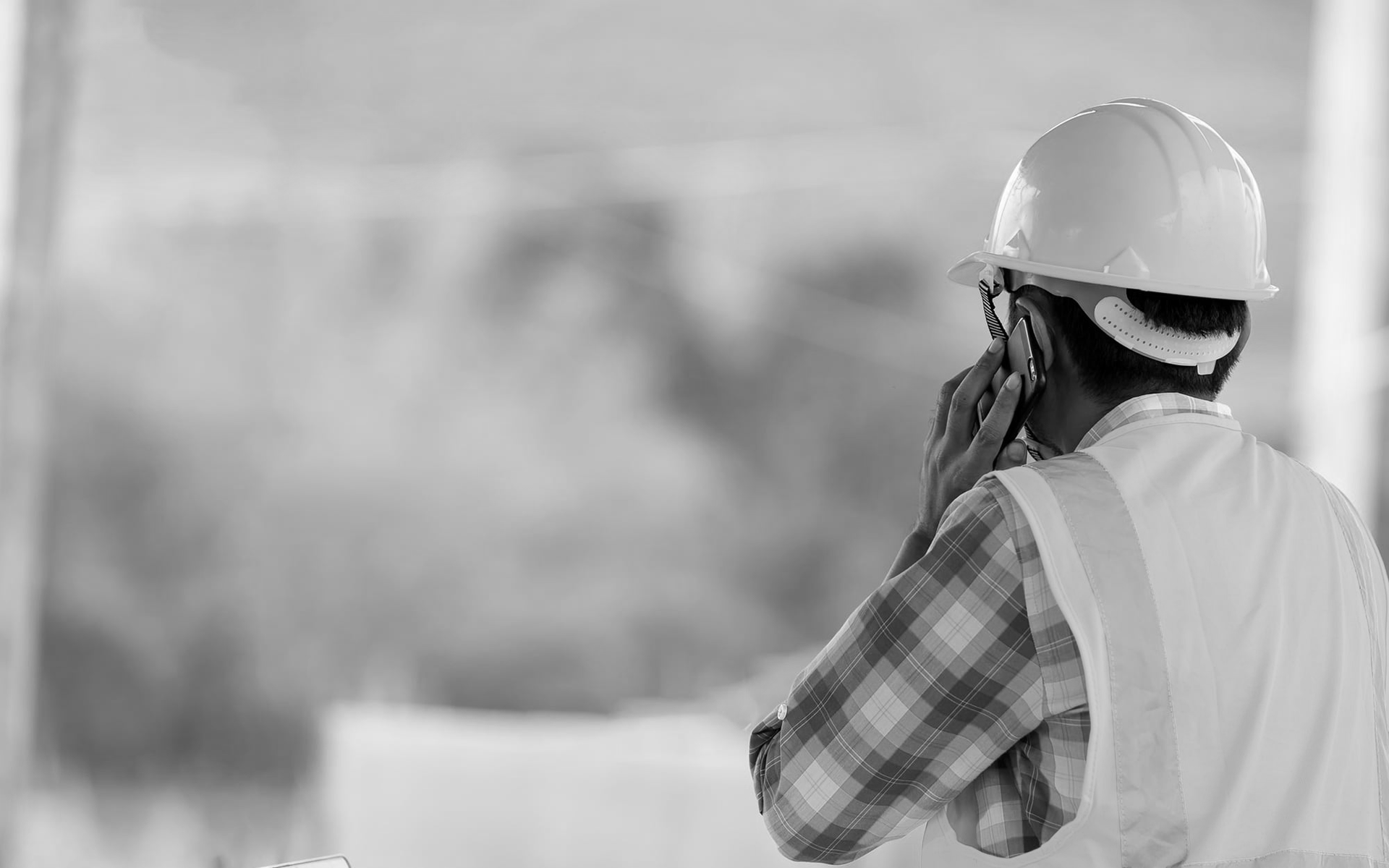 Worker in a hard hat and safety vest speaking into a radio at a construction site