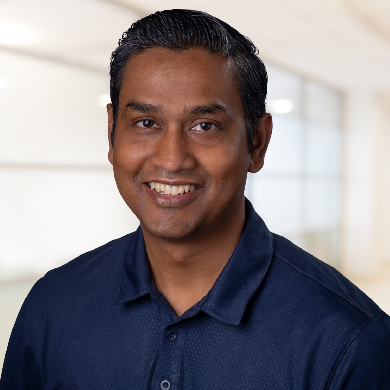 Smiling person in a navy shirt against a bright blurred office background