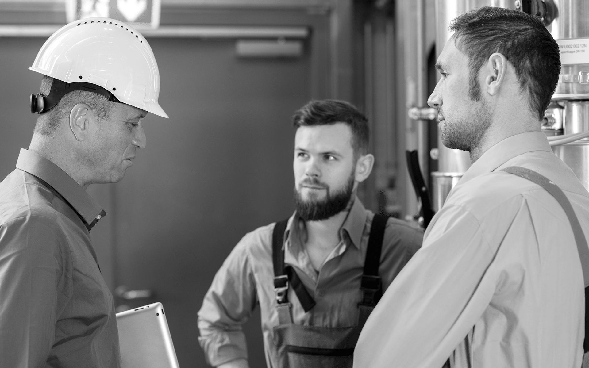 Three workers in hard hats and safety gear discussing on a construction site