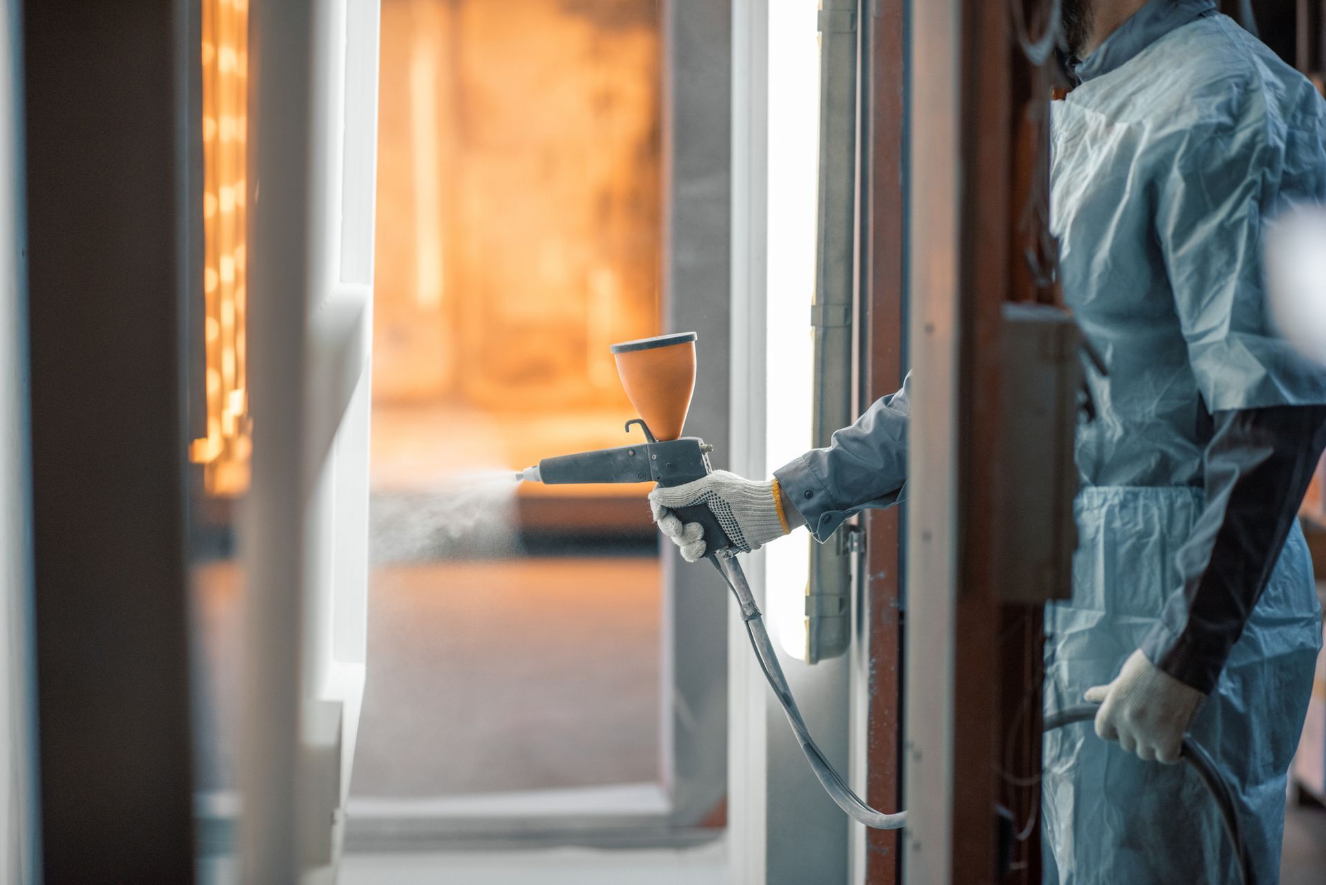 Person in protective suit spray painting inside industrial setting.
