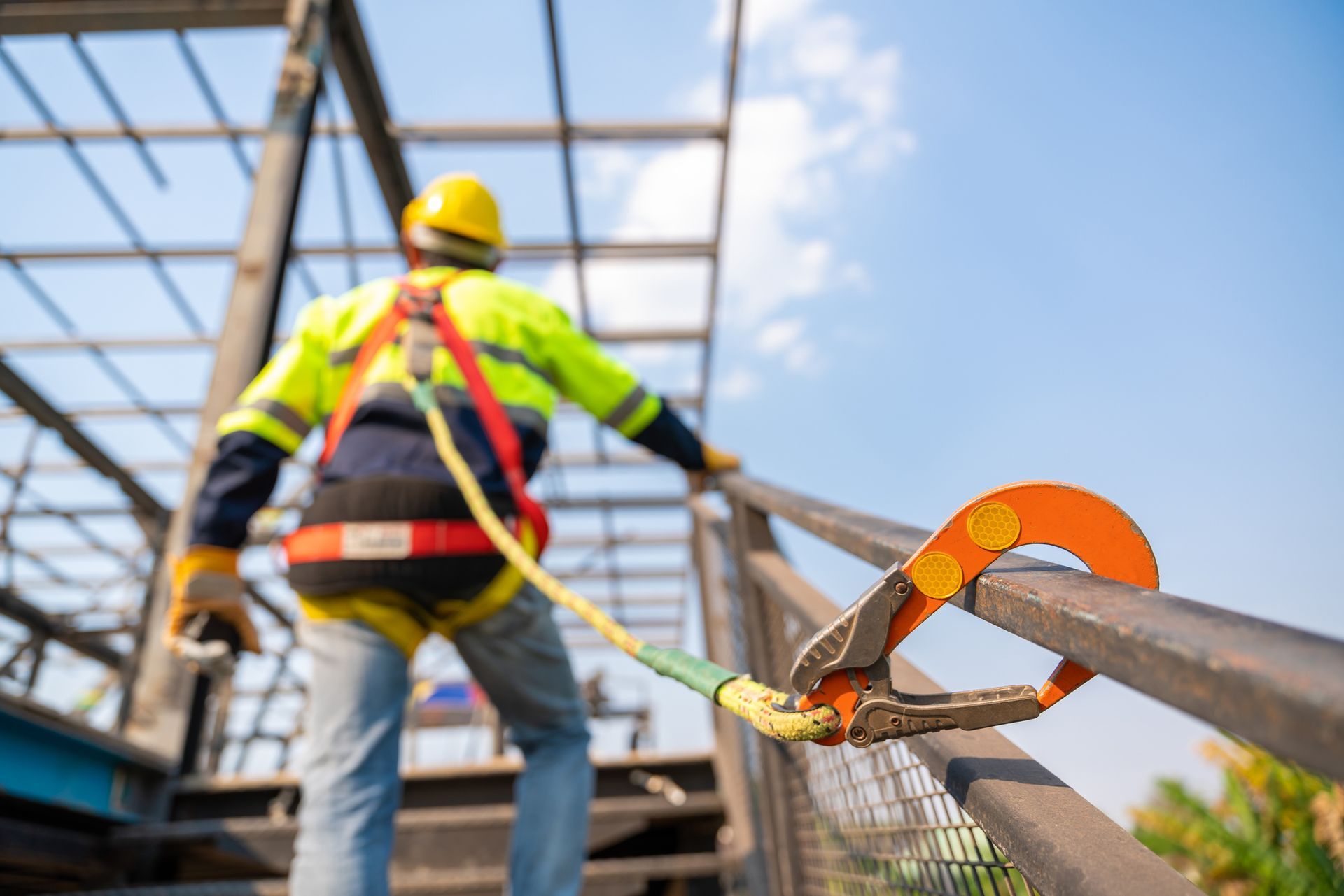Roofing contractor in safety gear climbing steel structure with harness and safety rope.