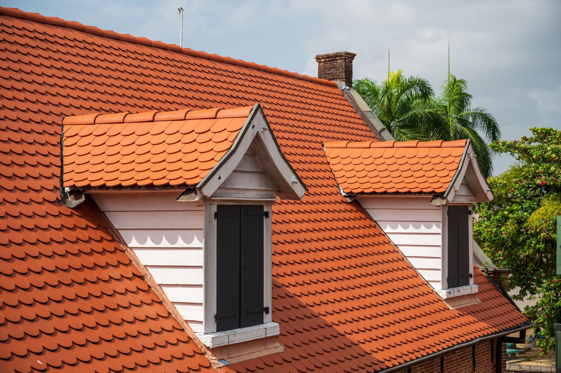 Red tile roof with three white dormers, black shutters, and a chimney.