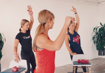 A person in activewear performs a standing knee-up exercise on a mat in a bright, modern living room.