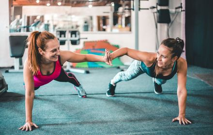 A group of twelve women posing together in a fitness studio, wearing athletic clothing and smiling at the camera.