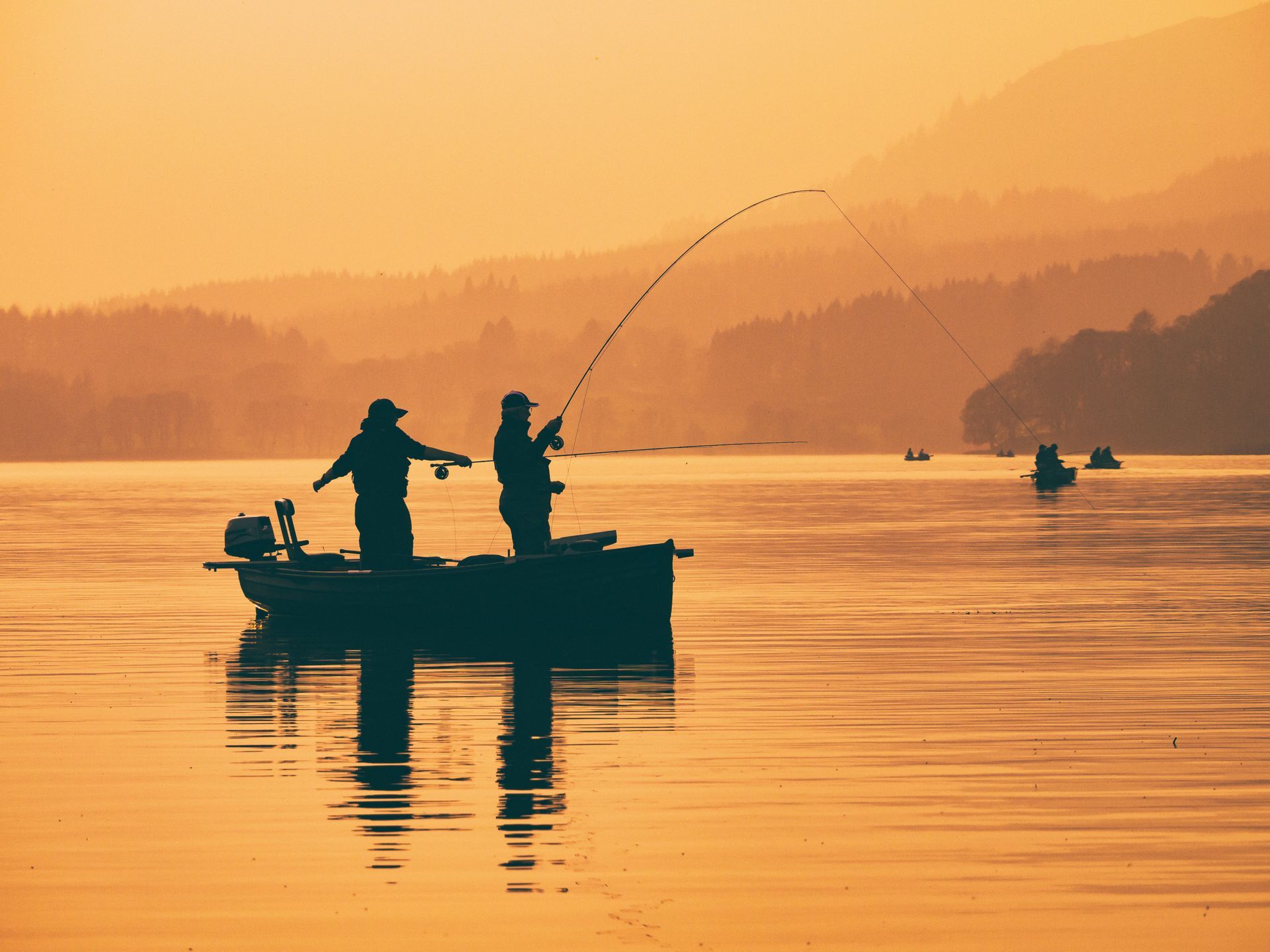 Two men are fishing in a boat on a lake at sunset.