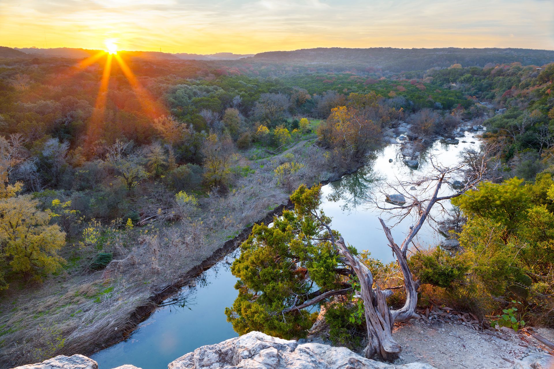 The sun is setting over a river surrounded by trees.