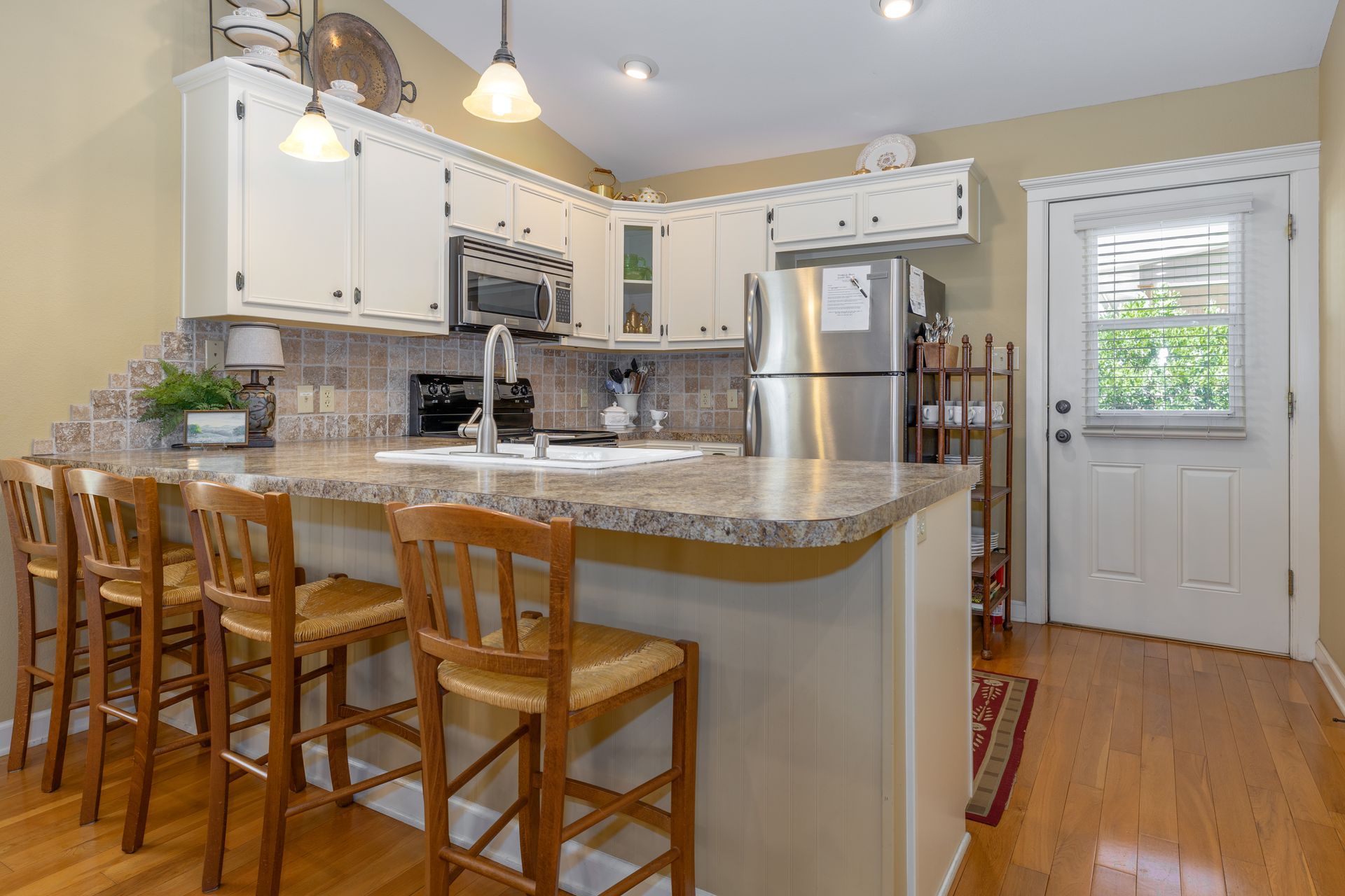 A kitchen with white cabinets , stainless steel appliances , granite counter tops , and wooden chairs.