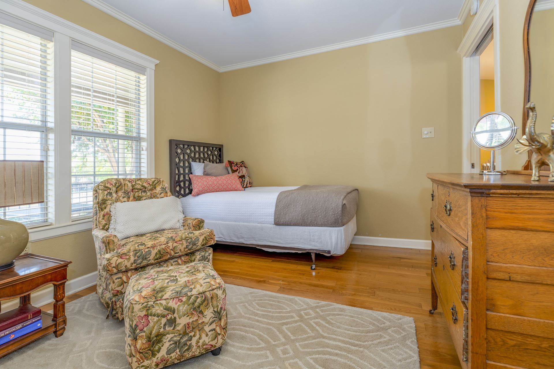 A bedroom with a bed , chair , dresser and mirror.