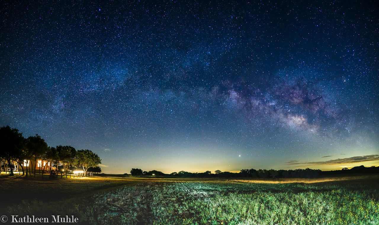 The milky way is visible over a field at night.