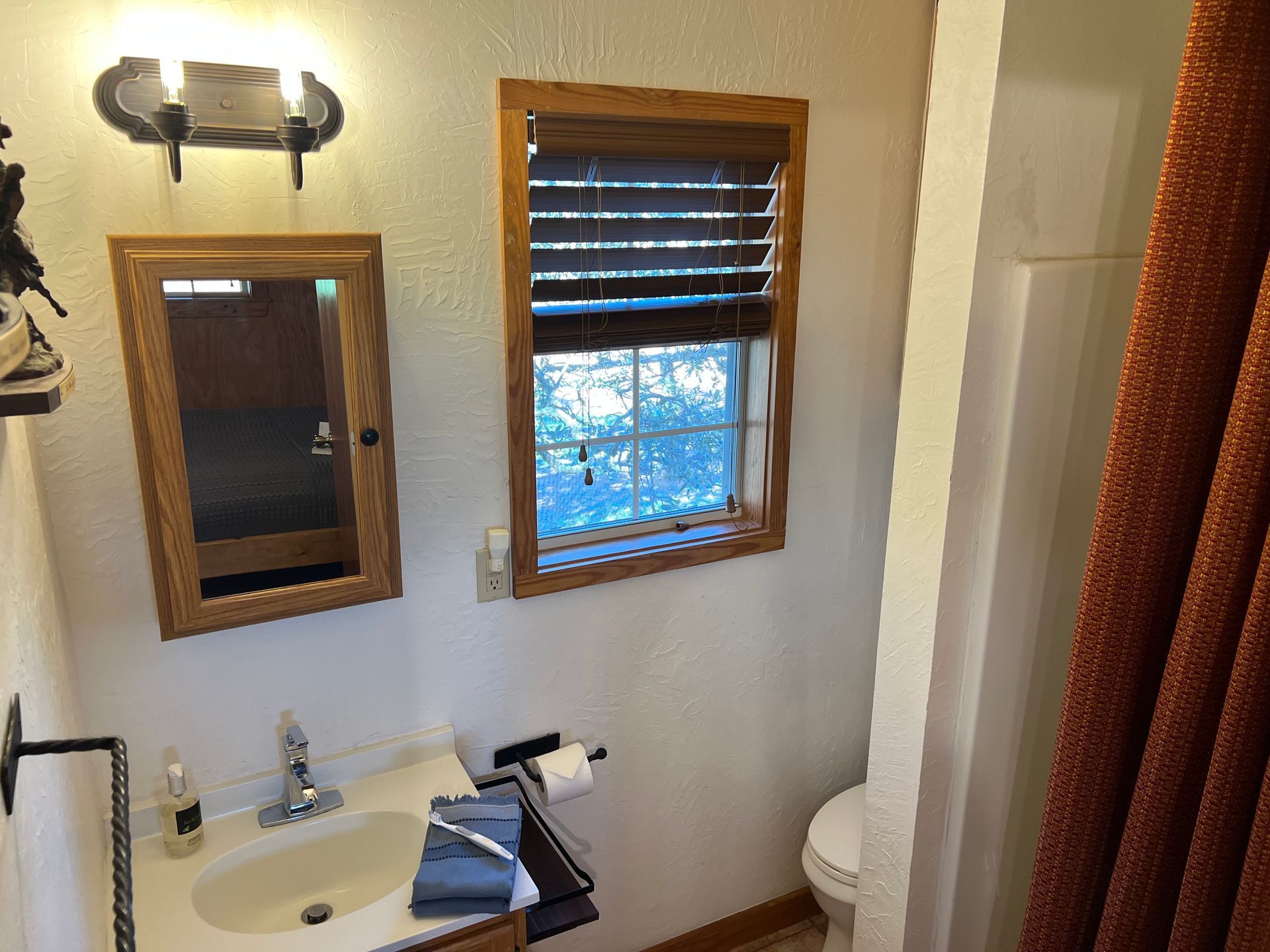 A bathroom with a sink , toilet , mirror and window.
