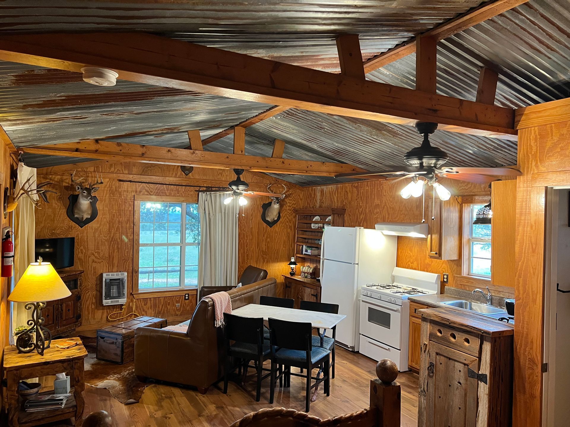 A living room and kitchen in a cabin with a ceiling fan.