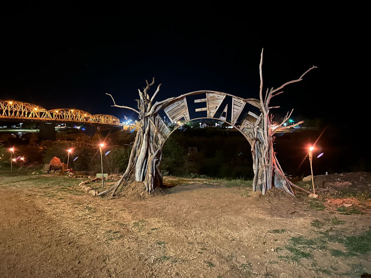 A wooden archway with a bridge in the background at night.