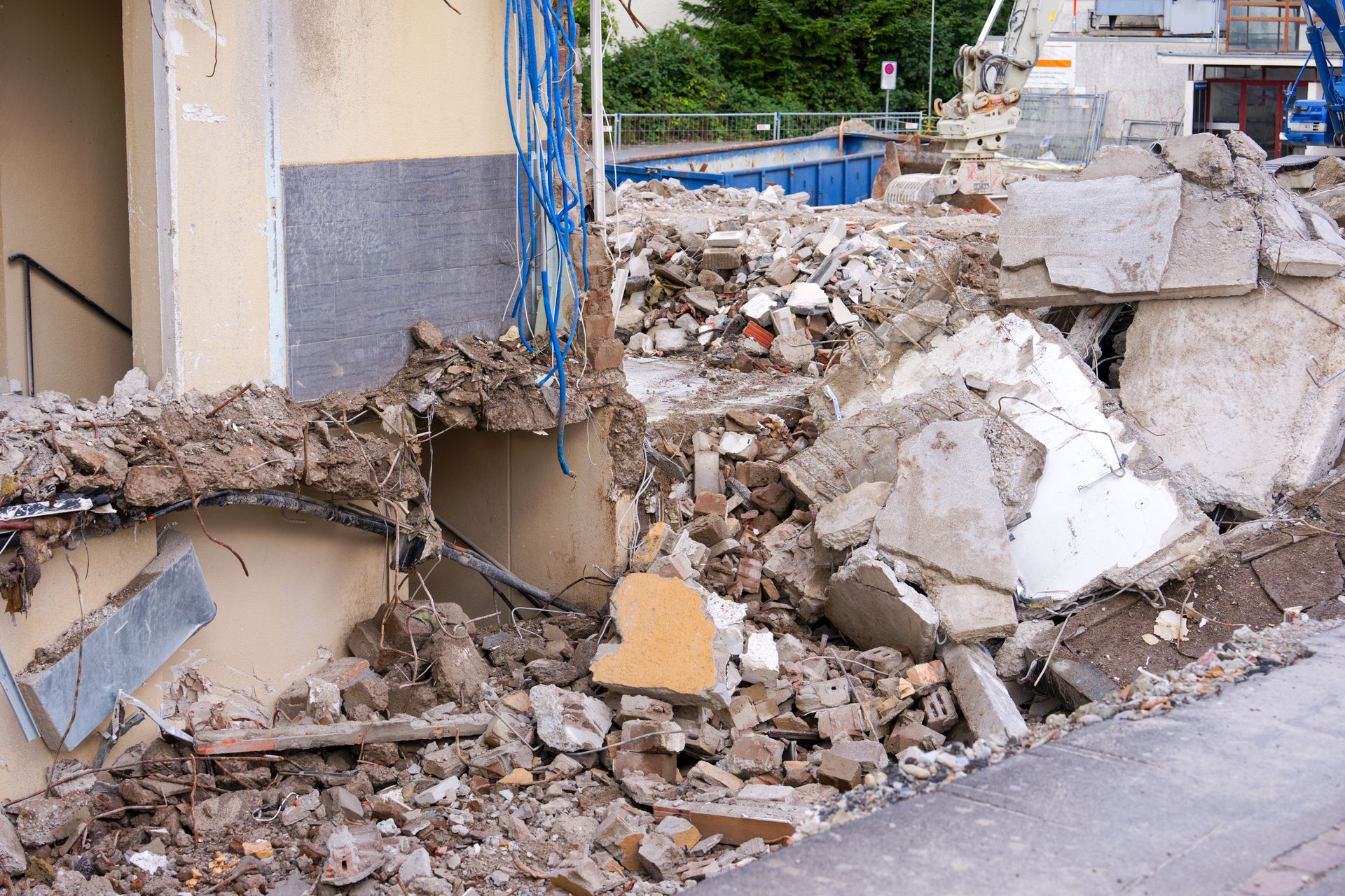 Debris from a building demolition piles against a wall and sidewalk. Wires and rubble fill the frame. Debris from a building demolition piles against a wall and sidewalk. Wires and rubble fill the frame.