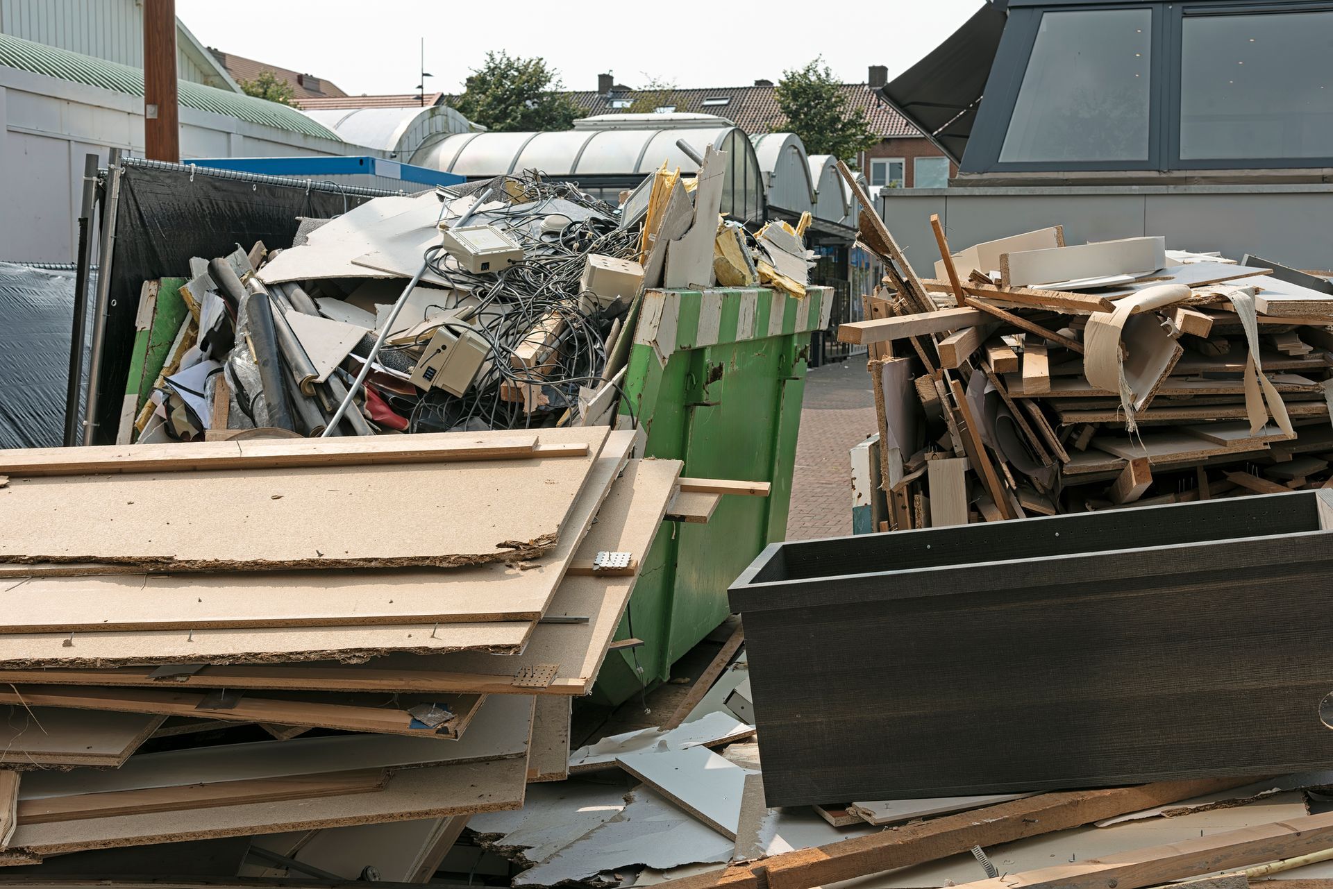 Pile of construction debris and scrap wood near a green dumpster.