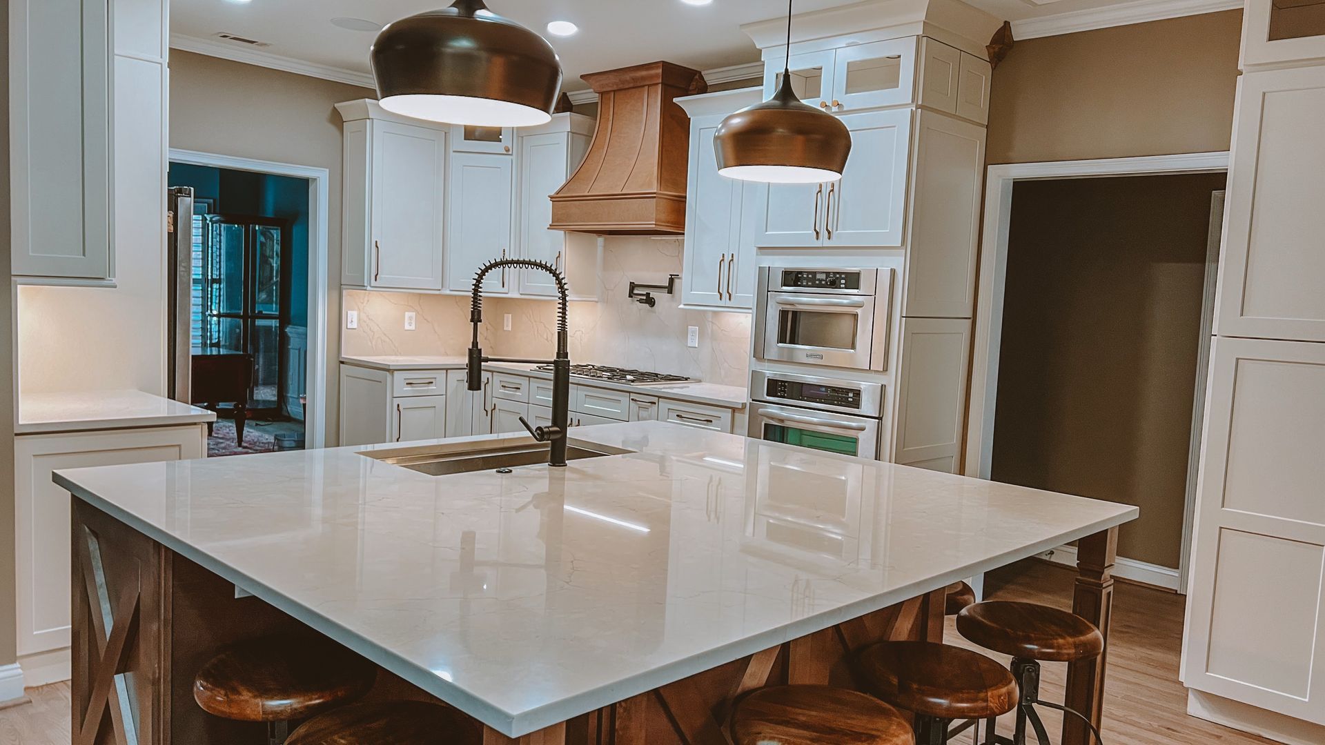 Kitchen with white cabinets, large island with seating, and bronze pendant lights.