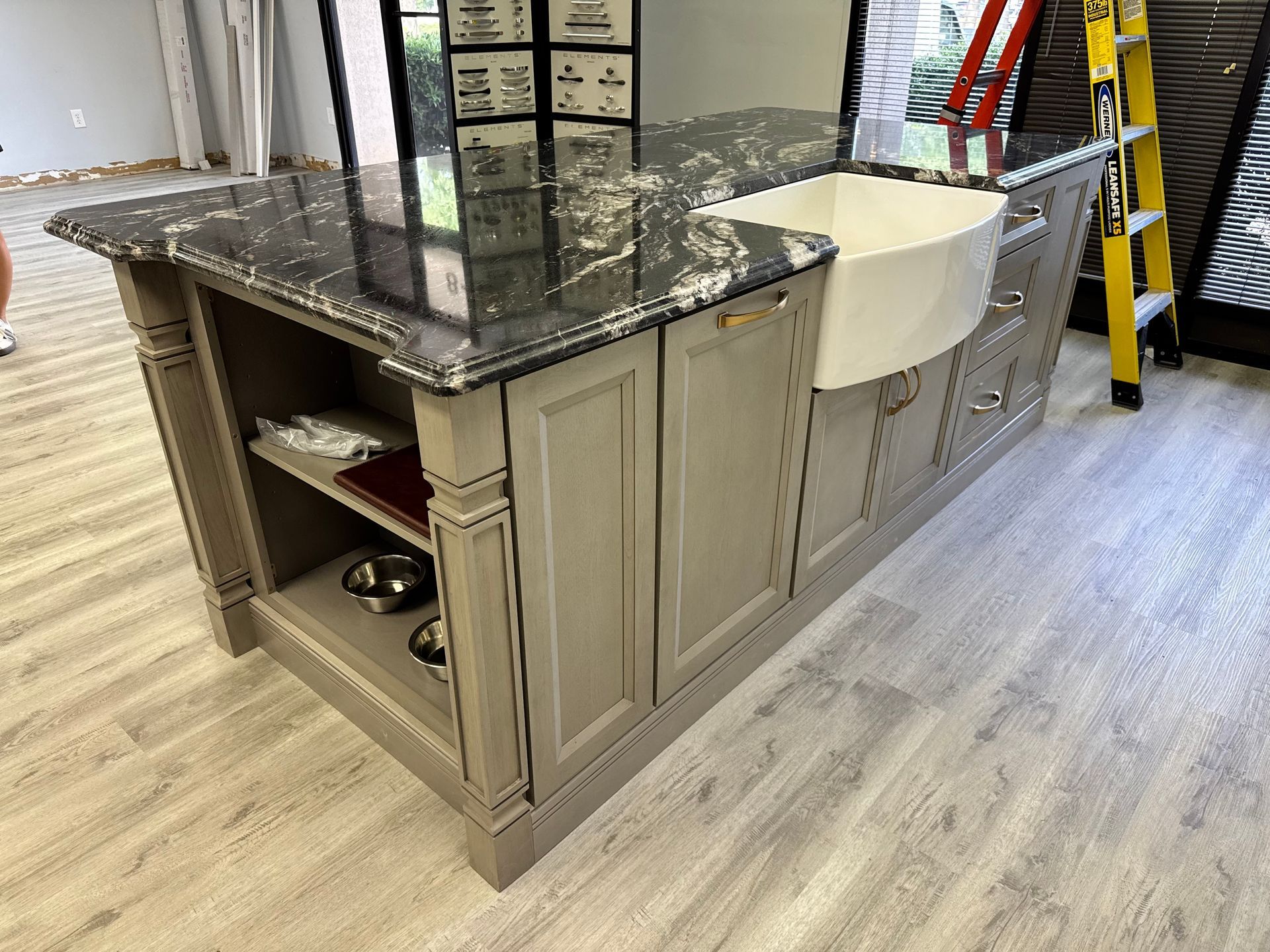 Kitchen island with granite countertop, farmhouse sink, gray cabinets, and open shelving.