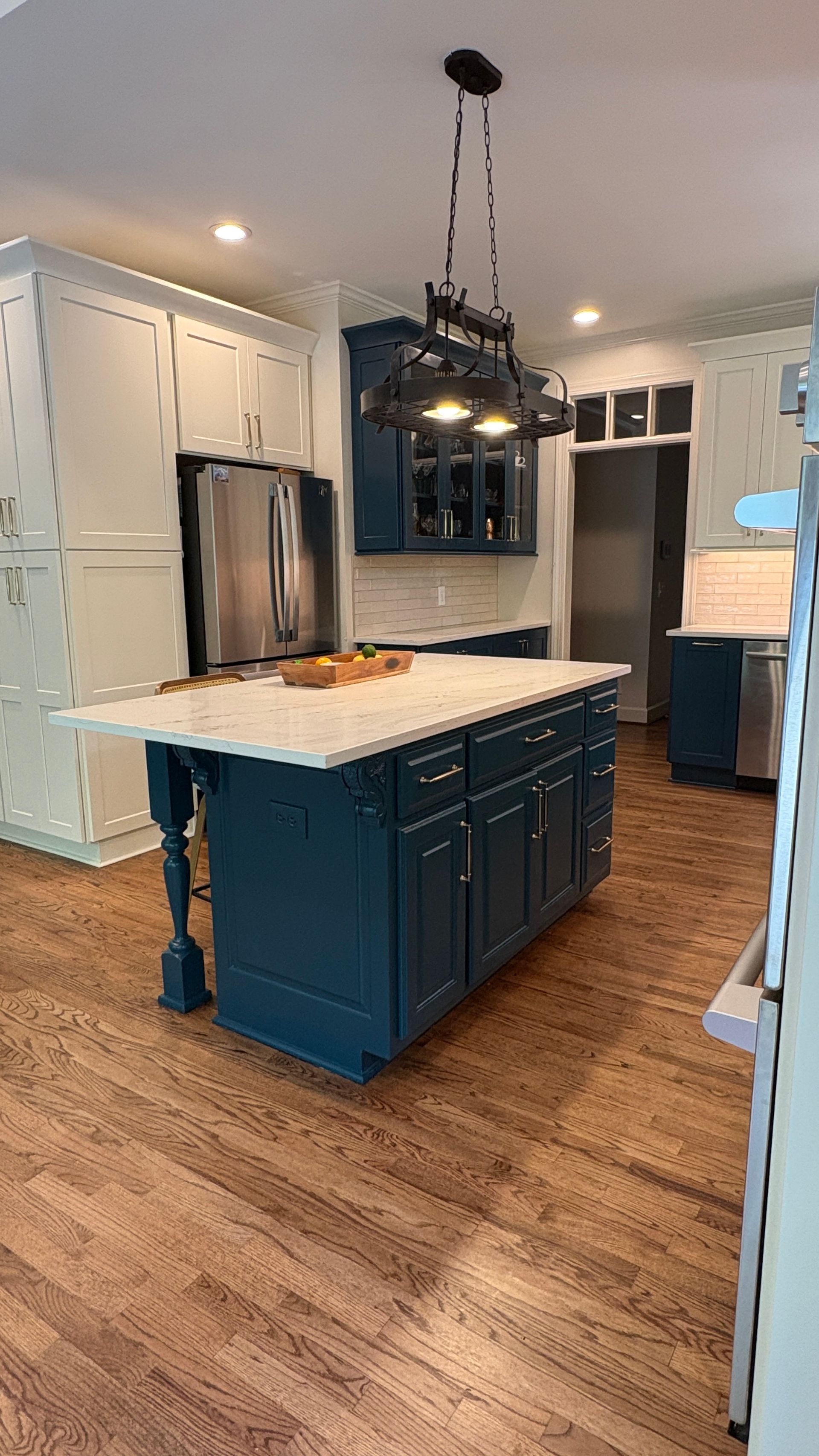 Blue kitchen island with white countertop, surrounded by white and blue cabinets, hardwood floors.