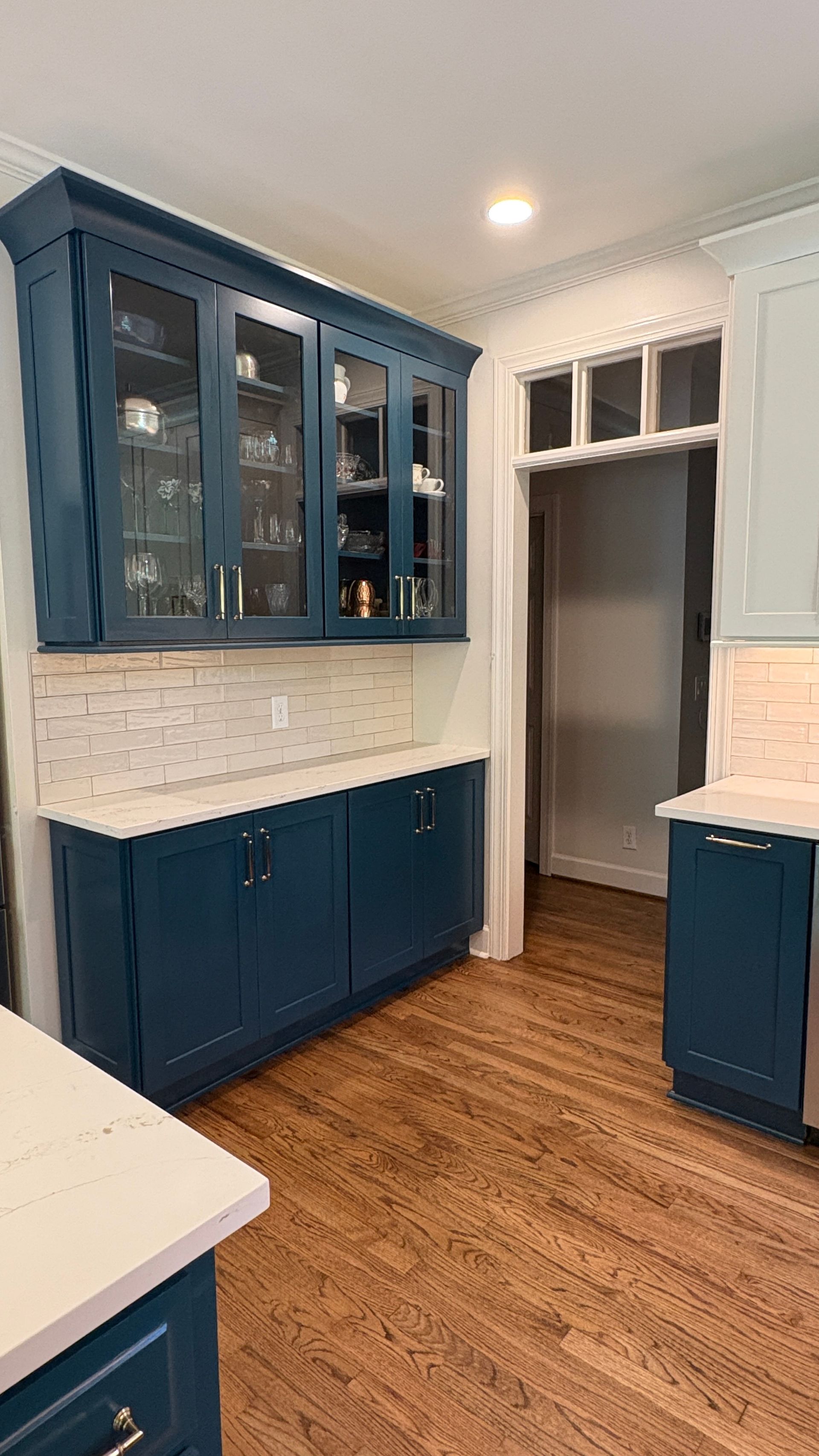 Blue kitchen cabinets with glass-front uppers and white countertops. Wooden floors.