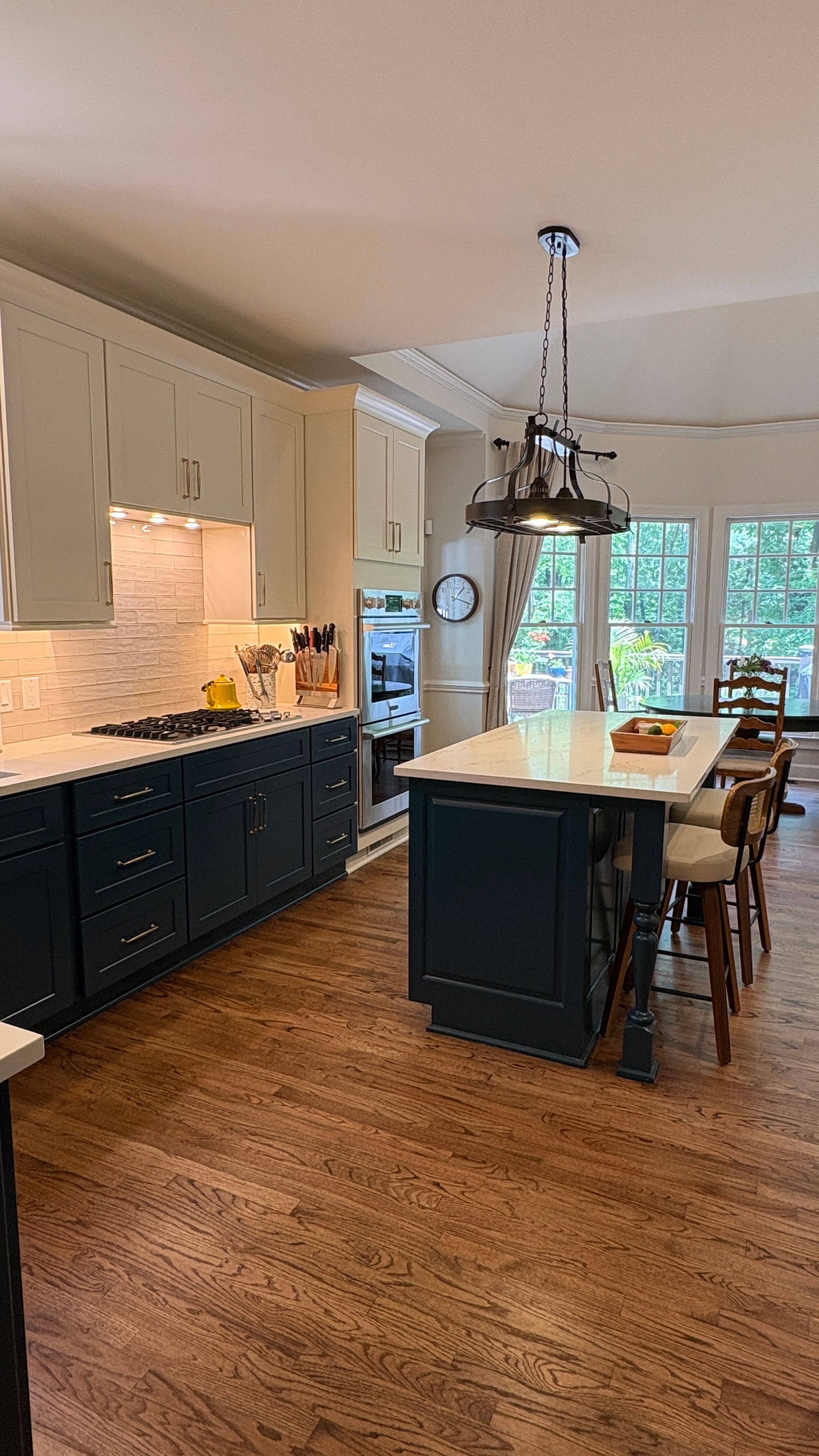 Kitchen with navy and white cabinets, island with stools, and hardwood floors.