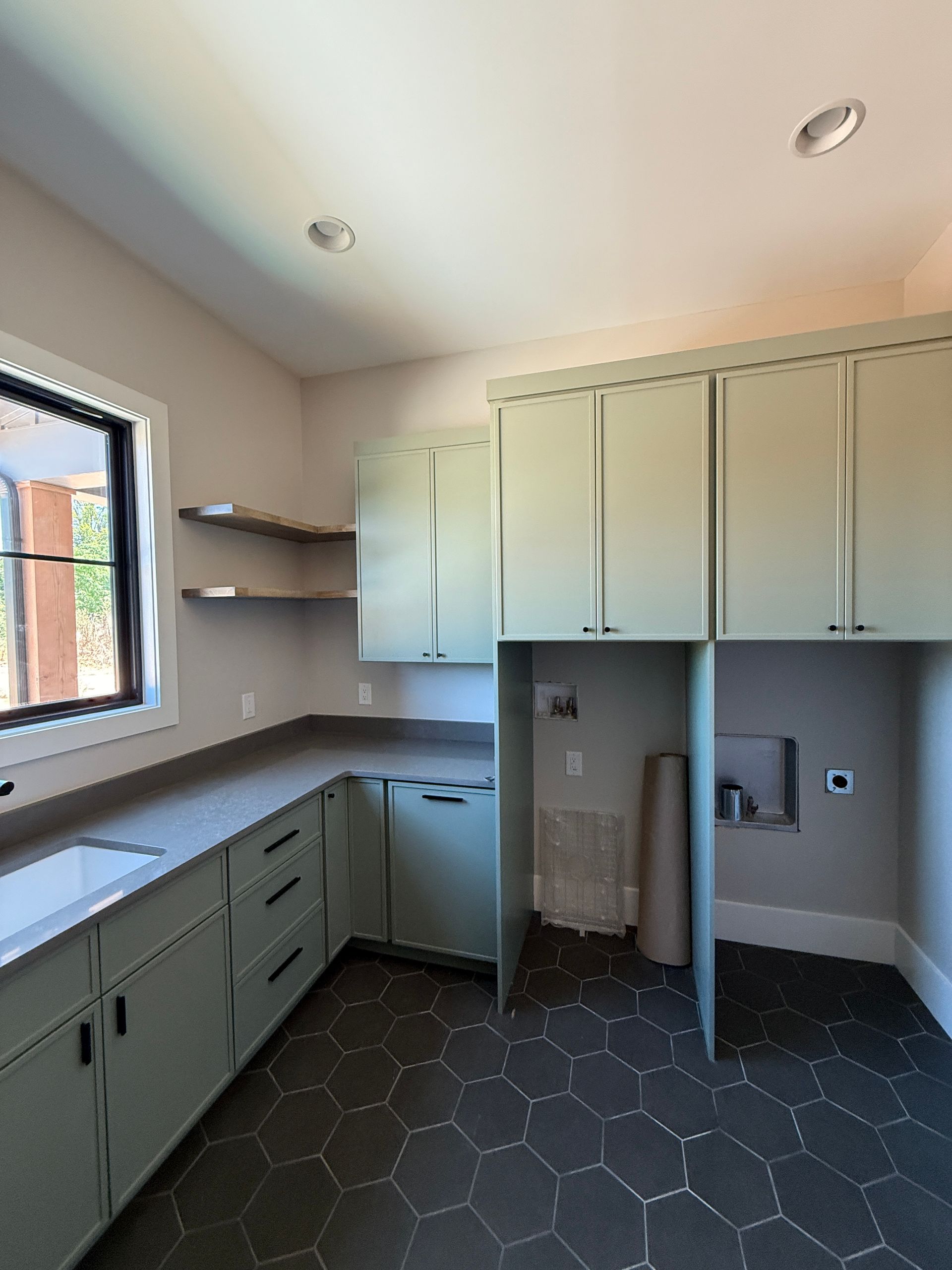 Laundry room with green cabinets, dark gray countertop, and hexagonal tiled floor.