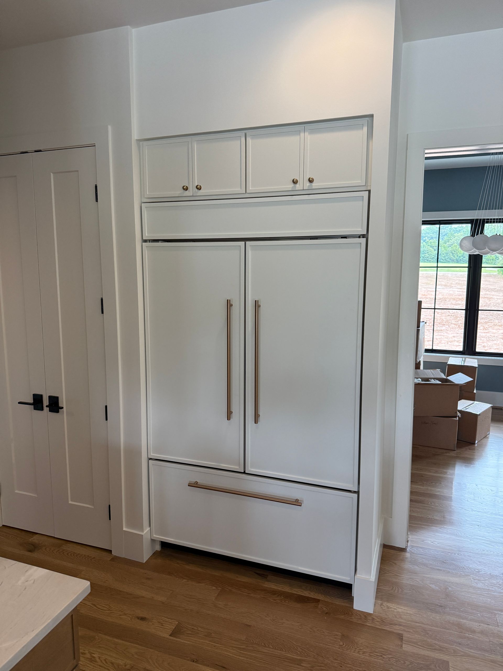 White built-in refrigerator with upper cabinets in a kitchen, next to a white door.