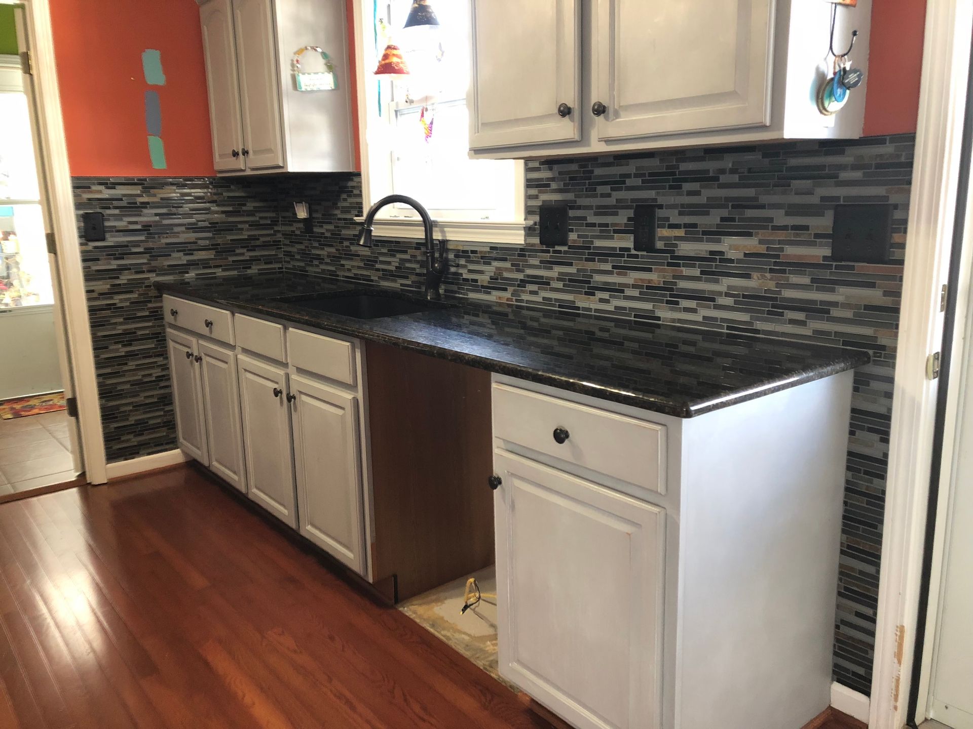 Kitchen with white cabinets, dark countertops, and mosaic backsplash.