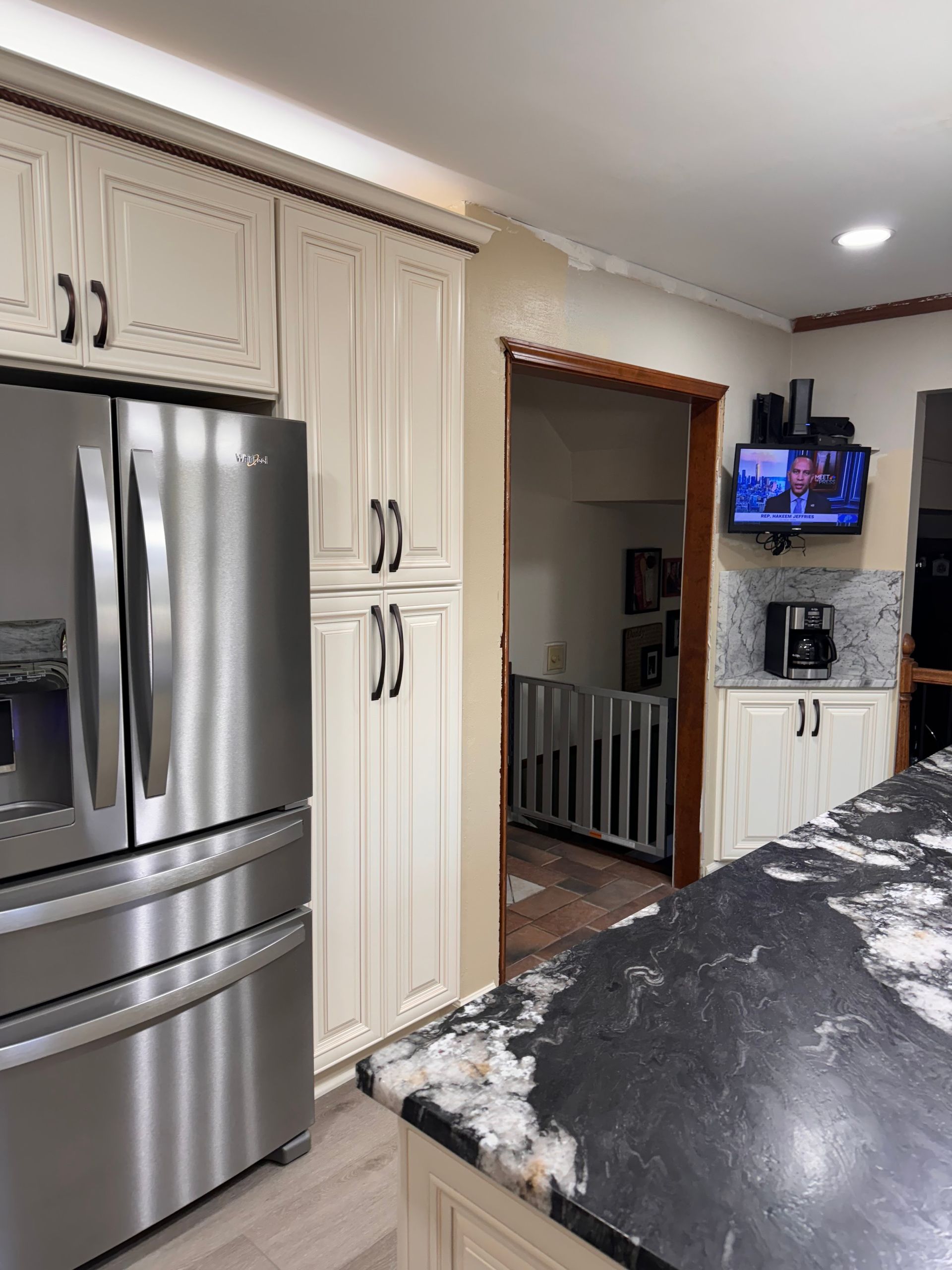 Kitchen with stainless steel fridge, white cabinets, and a doorway leading to stairs.
