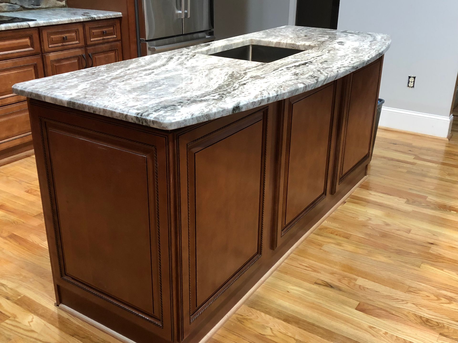 Kitchen island with a granite countertop and brown wooden cabinets. A sink is built in.