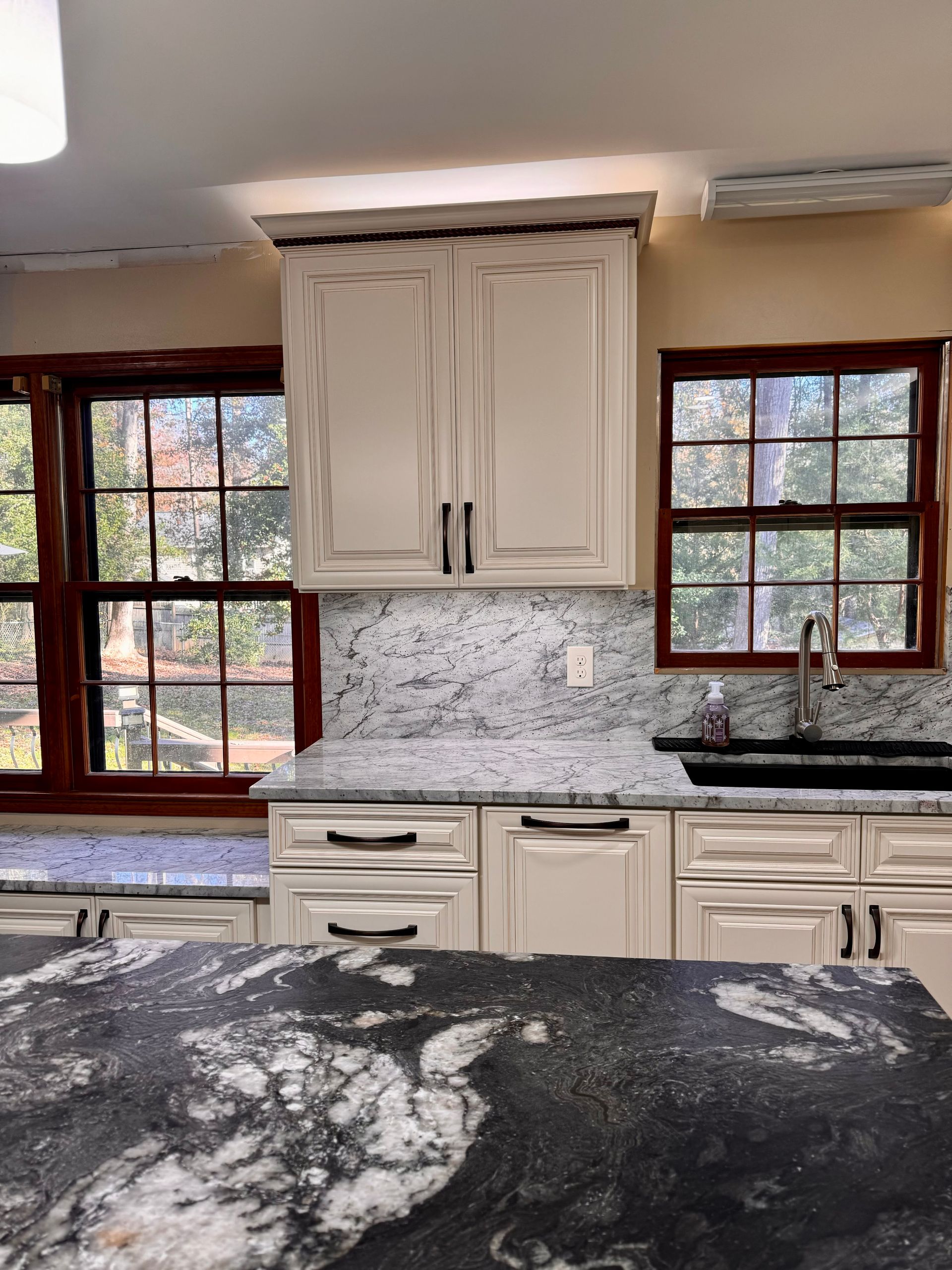 Kitchen with cream cabinets, granite countertops, and two windows.