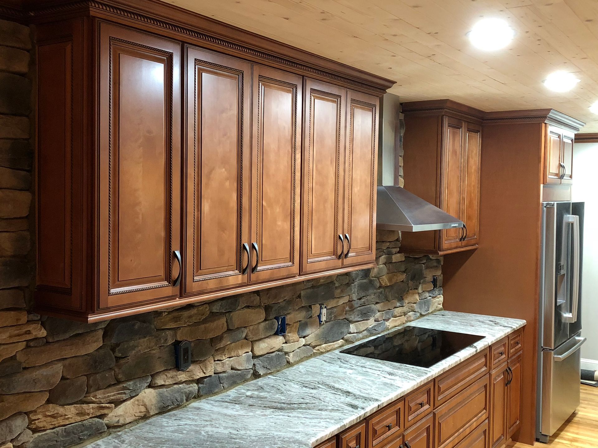 Kitchen with brown cabinets, stone backsplash, granite countertop, stainless steel appliances.