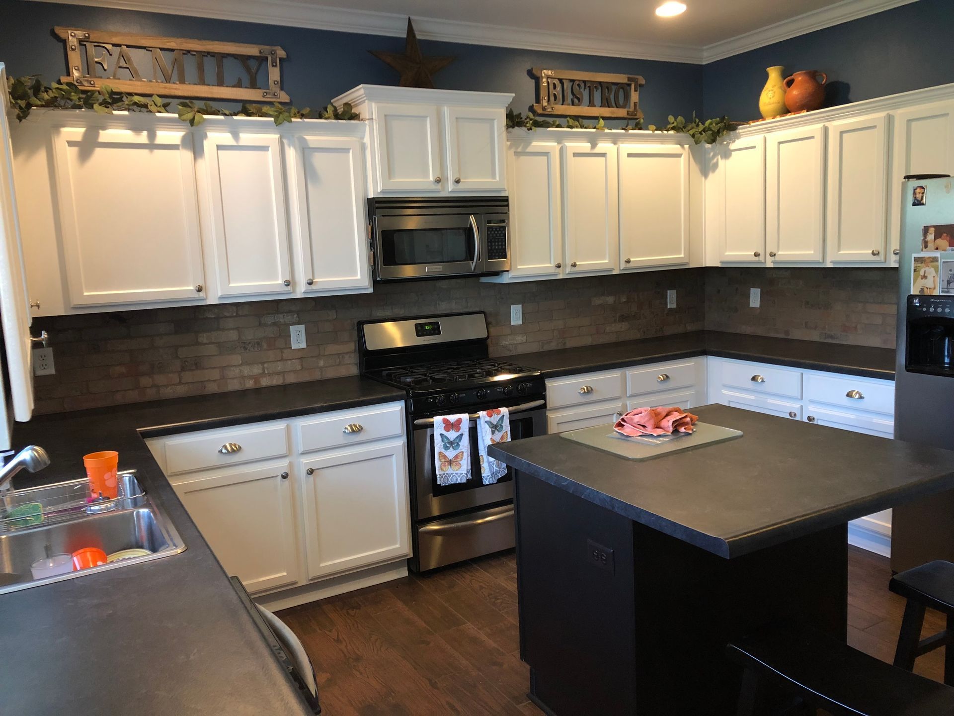 Kitchen with white cabinets, stainless steel appliances, dark countertops, and island.