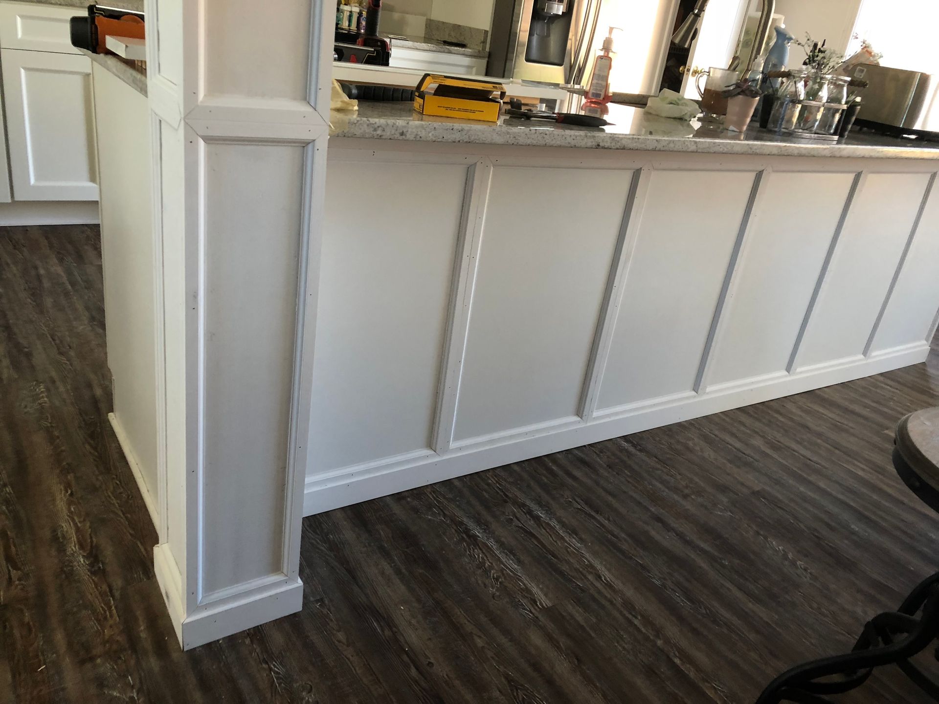 White kitchen island with vertical paneling and trim, contrasting dark wood-look flooring.