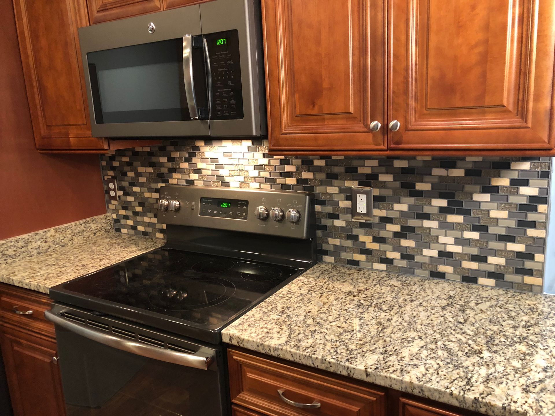 Kitchen with brown cabinets, stainless steel appliances, speckled countertops, and mosaic backsplash.