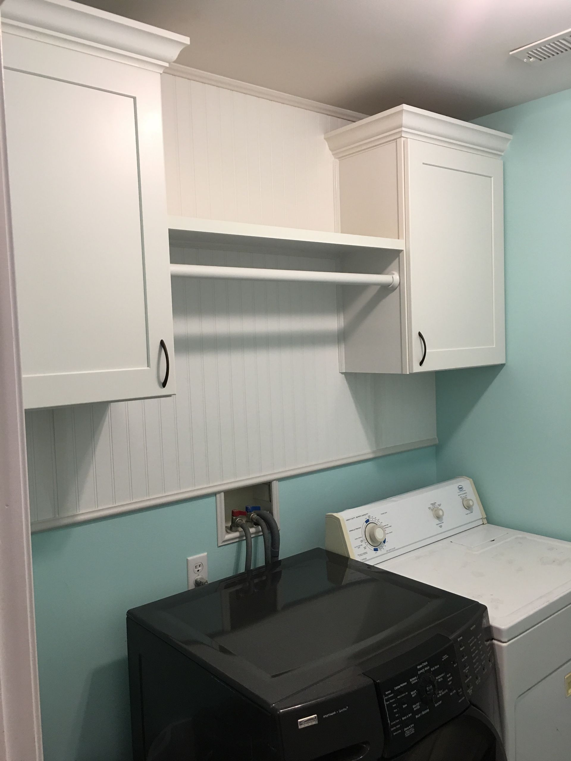 Laundry room with white cabinets, drying rod, and black washer and white dryer on a blue wall.