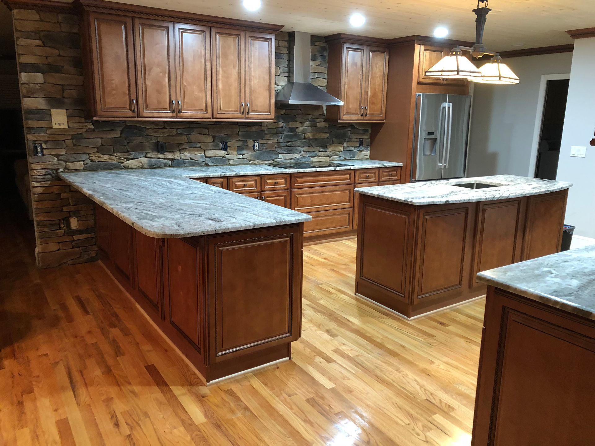 Kitchen with brown cabinets, stone backsplash, granite countertops, and hardwood floors.