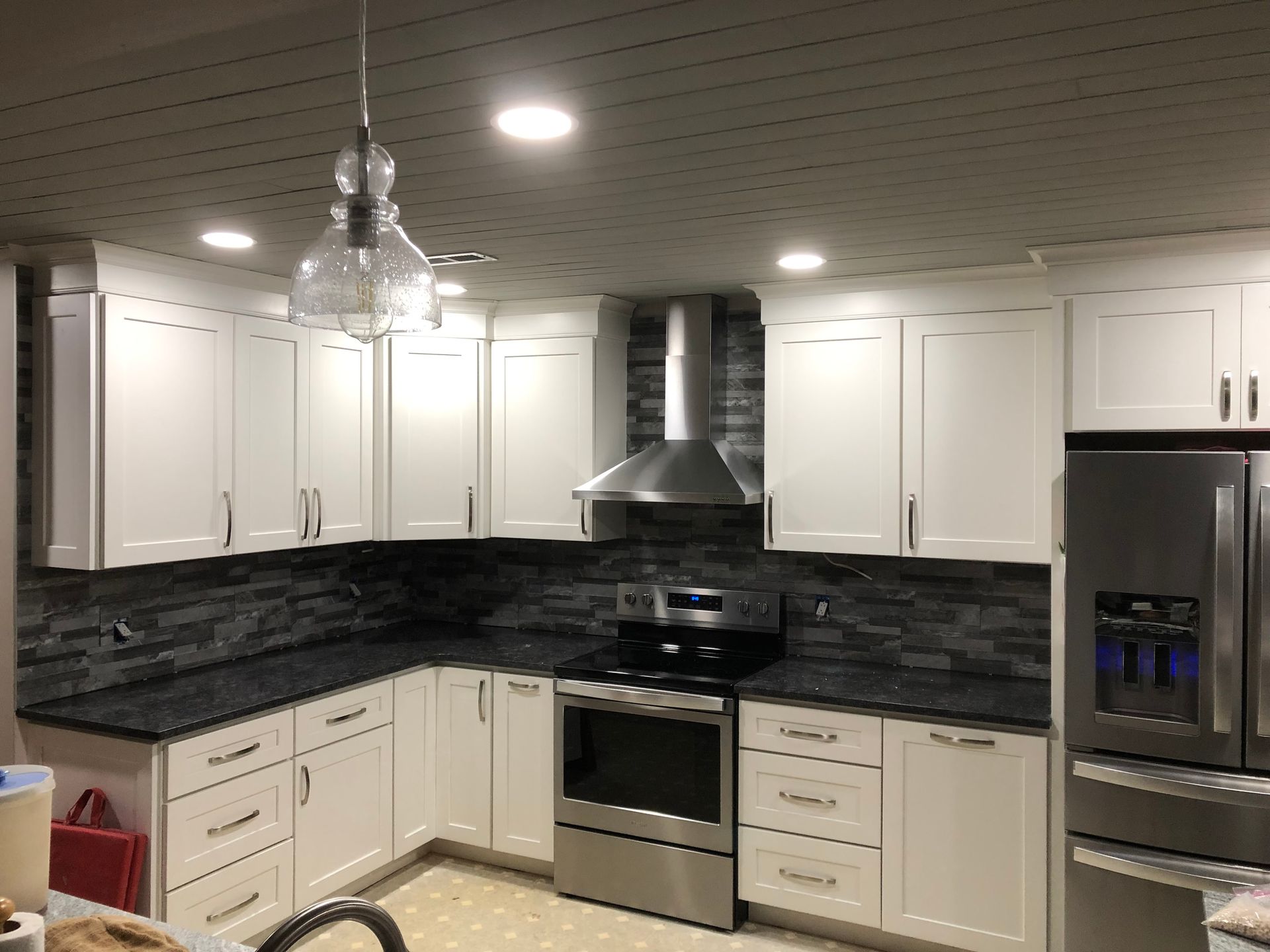 White kitchen cabinets, black countertops, stainless steel appliances, dark backsplash, and pendant light.
