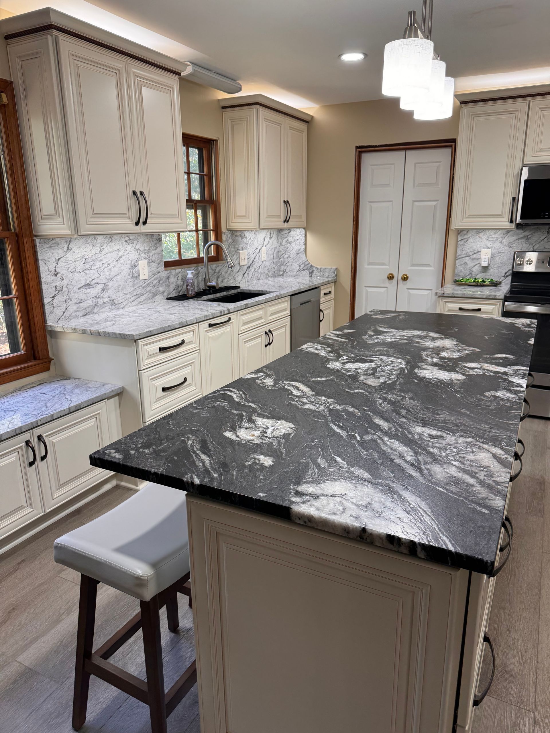 Creamy kitchen with dark countertop island and matching perimeter counters, light cabinets.
